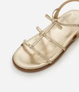 Sandalia plana dorada con tiras finas y detalle de lazos.