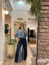 Blusa de jean fino con cuello alto, mangas largas con volumen y volados decorativos en los hombros. Presenta detalles de ribetes en terciopelo azul oscuro en el frente y los volados.