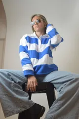 Sweater de punto a rayas horizontales azules y blancas, con cuello polo y cierre parcial con cremallera.