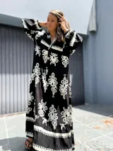 Vestido largo estilo túnica, color negro con estampado ornamental en blanco. Presenta cuello en V con botones y mangas largas amplias.