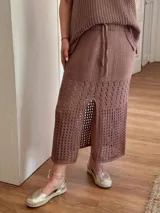 Pollera midi tejida en hilo de algodón, con diseño de calados en franjas horizontales, silueta recta, abertura frontal y cintura elástica con cordón ajustable.