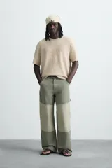 Camiseta de punto color beige claro, corte boxy fit, con cuello redondo y manga corta. Presenta un estampado central en tono similar que simula un efecto spray y acabados irregulares en los bordes.