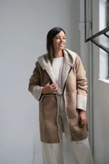 Tapado tipo gamuza con interior de corderito sintético, color beige con detalles en crudo. Presenta capucha, cierre frontal completo y puños con vuelta de corderito.