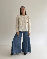 Blusa de color beige con bordados florales en el frente, detalle de volados verticales y mangas largas con puños elásticos.