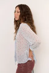 Blusa marrón semitransparente con estampado de lunares celestes, mangas largas abuchonadas, cuello en V con lazos y detalles de volados frontales.