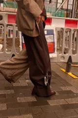 Pantalón de sastrería con diseño bicolor asimétrico, combinando una pierna en color marrón oscuro y la otra en beige, ambos con un sutil estampado de rayas diplomáticas. Presenta una silueta de corte recto y relajado, con cierre frontal y botón de nácar.