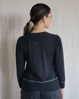 Remera blanca de manga larga con diseño de cuello en V y detalle de tablas frontales. Presenta mangas con sutil frunce en los hombros y puños rectos.