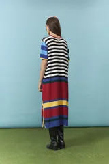 Vestido midi de algodón con diseño de rayas horizontales en color blanco y negro en el torso, mangas cortas con bloques de colores celeste, azul, verde y amarillo, y parte inferior con franjas anchas en rojo, amarillo y azul. Cuenta con cuello redondo ribeteado en rojo.