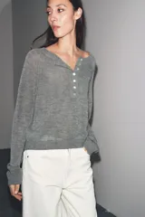 Jersey de punto color gris, con cuello redondo y abertura frontal con botones. Presenta mangas largas raglán y puños y bajo acanalados.