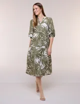 Vestido midi de silueta holgada en color blanco con estampado de hojas verdes. Presenta escote en V con cuello mao y botones frontales en la pechera, mangas tres cuartos abullonadas con puños elásticos y falda de corte evasé con niveles fruncidos.