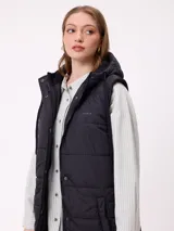 Chaleco largo acolchado color beige, con capucha forrada en sherpa, cierre frontal con cremallera y botones a presión, y bolsillos laterales.