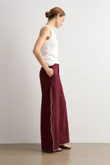 Pantalón ancho color bordó de talle alto, con abertura lateral decorada con ribete contrastante y cierre de botones tipo nudo chino.