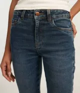 Pantalón bootcut de jeans azul con cintura alta, trabillas y cierre con botón y cremallera. Posee bolsillos delanteros y traseros, y detalle de encaje en el lateral de la parte baja.