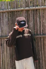 Buzo de tejido de punto color marrón con cuello polo, manga larga y estampado frontal con el nombre de la marca en color crema.