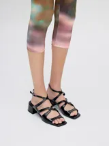 Sandalias de cuero con acabado charol color bordó, con punta cuadrada, tiras onduladas en el empeine y correa ajustable con hebilla en el tobillo. Cuentan con un taco bajo forrado.