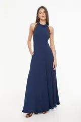 Vestido largo azul marino, de corte fluido, con escote halter, detalles trenzados en los hombros, bolsillos laterales y tajo profundo en la pierna.