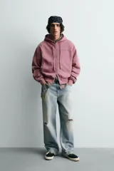 Sudadera tipo hoodie con cierre frontal de cremallera, diseño boxy fit, capucha ajustable con cordones, mangas largas con puños elásticos y bolsillos laterales. Presenta un acabado con efecto lavado.