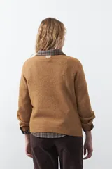 Sweater de tejido suave color tostado, con cuello redondo y detalle de flores bordadas en relieve en la parte superior del pecho. Presenta un corte relajado y mangas largas con puños ajustados.