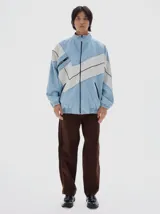 Campera de denim estilo deportivo con diseño de paneles en tonos azul claro y blanco, cuello alto, cierre frontal y bolsillos laterales con cierre. Presenta corte oversized con puños y cintura elásticos.