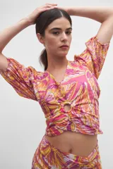 Blusa crop top rosada con estampado floral en tonos amarillos, naranjas y blancos, con escote en V, mangas abullonadas cortas y detalle de aro forrado en el centro del pecho con fruncidos.