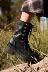 Borcego de caña corta confeccionado en cuero negro, con diseño de cordones y ganchos metálicos, cierre lateral y suela de plataforma dentada.