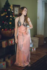 Vestido largo con estampado tie-dye en tonos violeta y fucsia, escote en V con detalles bordados dorados, cut-outs laterales bajo el busto y tirantes finos que se cruzan y atan en la espalda.