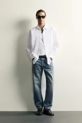 Jeans regular fit de mezclilla negra con efecto lavado, corte recto y tiro medio. Cuenta con diseño de cinco bolsillos y cierre frontal con cremallera y botón.