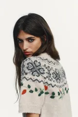 Jersey de punto de cuello redondo y manga corta, color beige con diseño de jacquard geométrico y bordados de flores y hojas en tonos rojos y verdes.