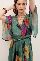 Vestido largo verde con estampado floral multicolor, escote en V cruzado, mangas amplias tipo capa y detalles metalizados.