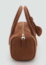 Bolso de mano tipo bowling de cuero gamuzado color marrón, con dos asas cortas y detalle de tiras con nudo y flecos colgantes en un lateral. Cierre superior con cremallera.