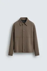Sobrecamisa negra de corte boxy fit en tejido compacto, con cuello solapa, manga larga con puño abotonado, bolsillos frontales aplicados y cierre frontal de botonadura.