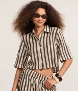 Camisa corta de algodón texturizado con diseño de rayas verticales en tonos beige y negro, cuello inglés y mangas cortas.
