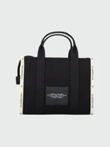 Bolso tote Marc Jacobs modelo The Jacquard, confeccionado en tejido de lona negro con detalles en blanco. Presenta el logo de la marca y la inscripción 'THE TOTE BAG' en el frente, con doble asa superior y correa ajustable extraíble.