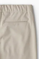 Pantalón de corte relajado en tejido suave, color beige, con cintura elástica, pliegues frontales, bolsillos laterales y bolsillos traseros ribeteados.