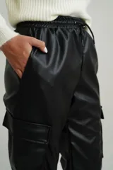 Pantalón babucha negro de cuero sintético con cintura elastizada con cordón ajustable, bolsillos laterales y bolsillos tipo cargo con solapa en los laterales de las piernas.