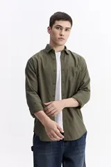 Camisa de manga larga con textura, color verde oliva, con cuello clásico, cierre frontal con botones y bolsillo en el pecho.