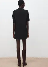 Vestido corto de punto negro con cuello alto y detalle de botones metálicos en el hombro.