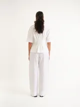 Blusa blanca de manga corta y cuello redondo, con diseño de rayas verticales texturizadas y detalles sutiles de flecos.