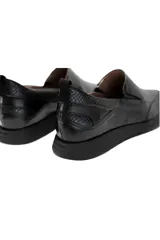 Zapatillas slip-on de cuero negro con textura sutil símil piel de reptil, inserciones elásticas laterales y suela flexible.