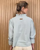 Blusa blanca de algodón con escote en V y cuello mao. Presenta mangas largas abullonadas con puños acampanados y fruncidos.