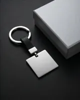 Llavero de acero con placa cuadrada pulida y correa de cuero sintético negro. Incluye un sistema de sujeción metálico para llaves.