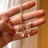 Collar dorado con dije de letra M, con piedras blancas, rojas y perlas engarzadas.