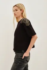 Remera de algodón color negro, de corte holgado y manga corta, con detalle de bordado en forma de plumas en los hombros.