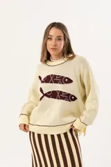 Sweater color manteca de tejido de punto con cuello redondo y ribete marrón. Presenta dos peces marrones tejidos en el frente con detalles bordados a mano.