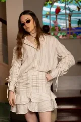 Falda corta de tiro alto con diseño de frunces en la parte frontal y doble volado en el ruedo. Presenta un estampado de rayas verticales en tonos neutros.