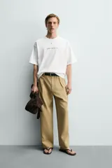 Camiseta blanca de corte relajado, con cuello redondo, manga corta y estampa frontal de texto pequeño en marrón.
