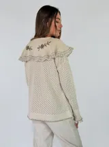 Saco tejido de punto color azul con diseño calado, cuello grande con bordados florales en tono crudo, volados decorativos y cierre frontal con un botón.