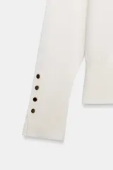 Jersey de punto liso con cuello redondo y manga larga. Presenta detalle de botones decorativos en los puños.