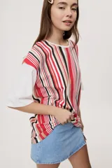 Remera oversize de manga corta con diseño de rayas verticales en tonos rojos, negros, blancos y tostados, y mangas blancas lisas.