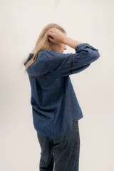 Camisa de jean azul oscuro con cuello mao, botones frontales, mangas largas abullonadas con puños elásticos y detalles bordados en color marrón en los hombros y mangas.